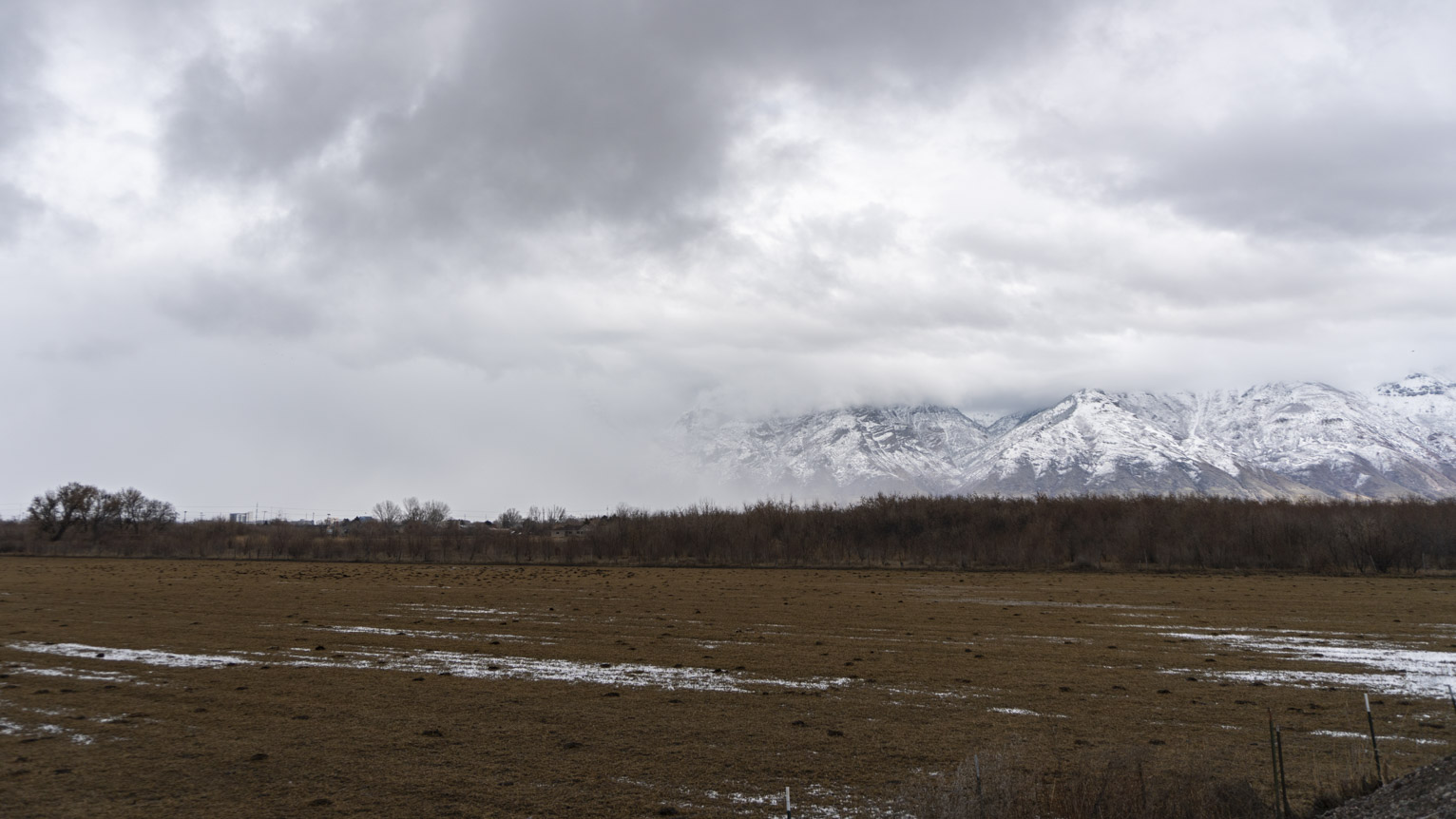 A coming snowstorm obscures the mountains above some farmland